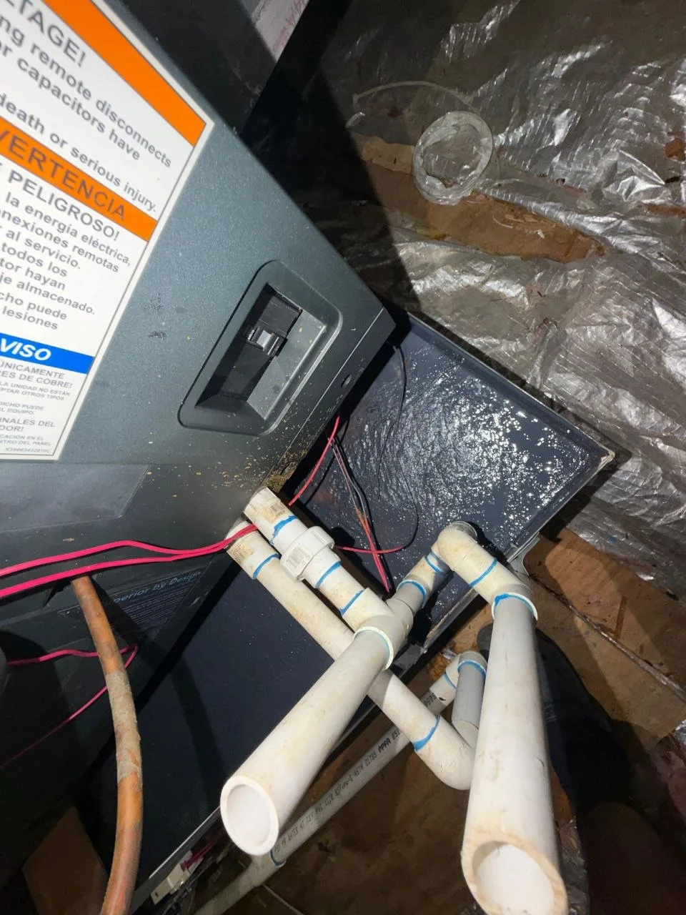 PVC condensate manifold and trap assembly at the attic air handler, with moisture visible on the pan below