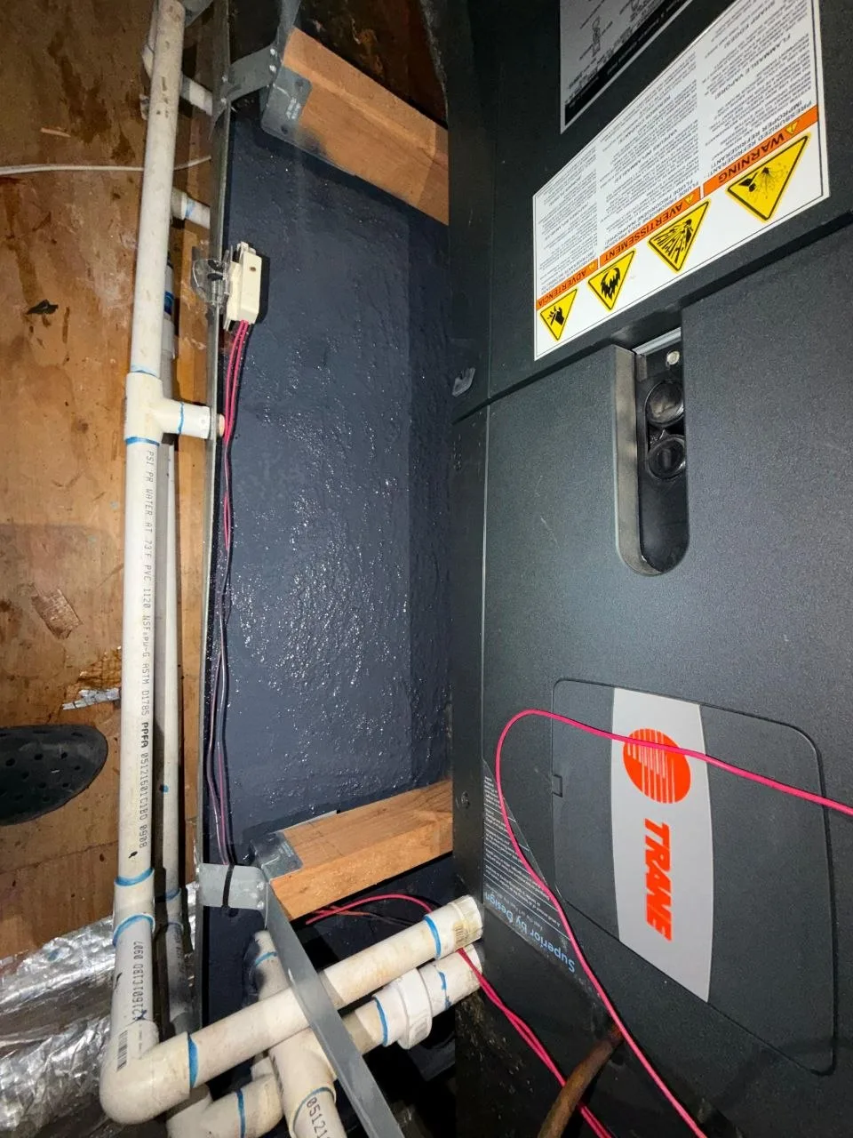 Emergency drain pan under a Trane air handler coated in an even layer of dark Plasti Dip rubber sealant