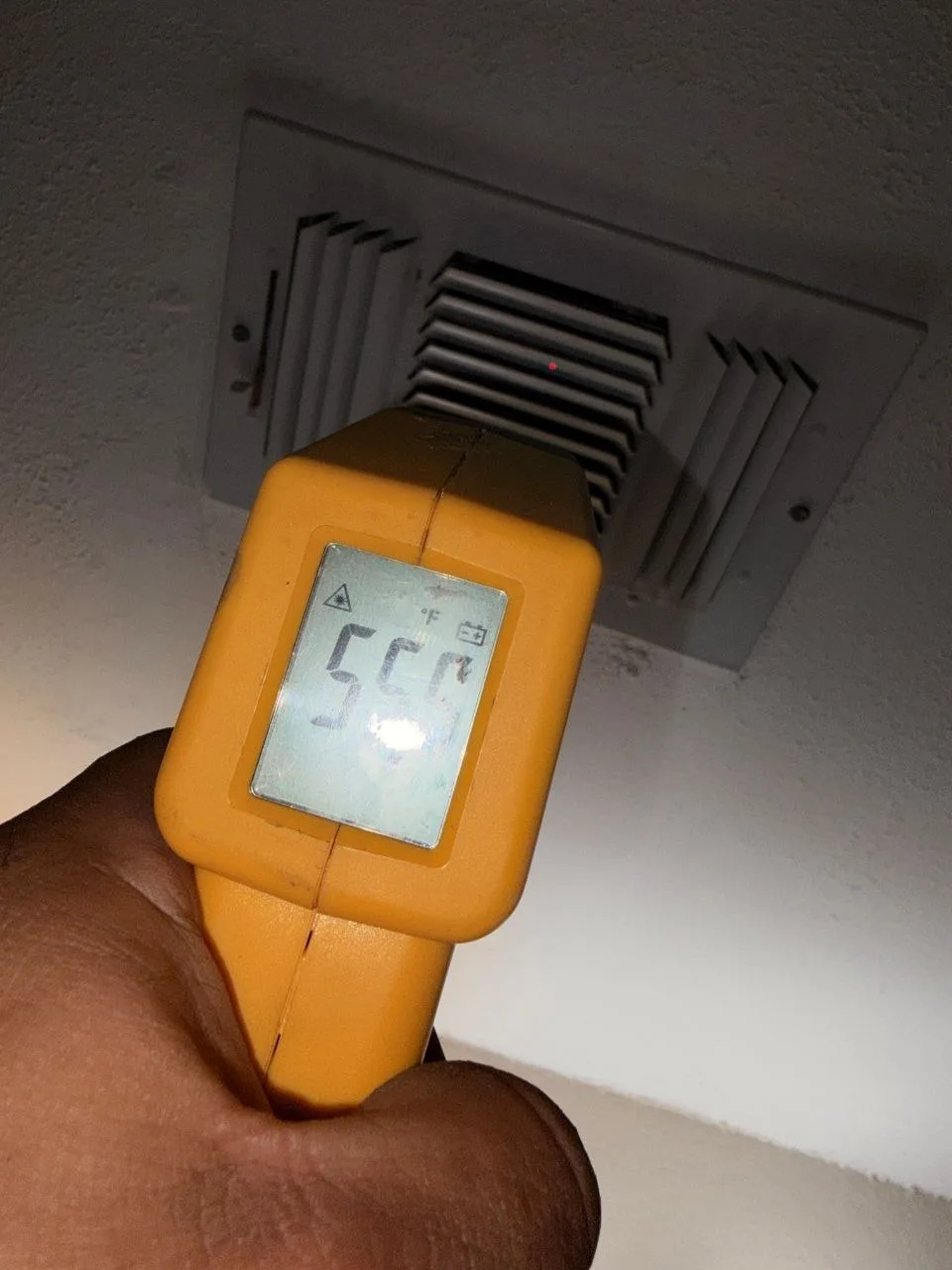 Infrared thermometer held at a supply vent during the post-repair performance check