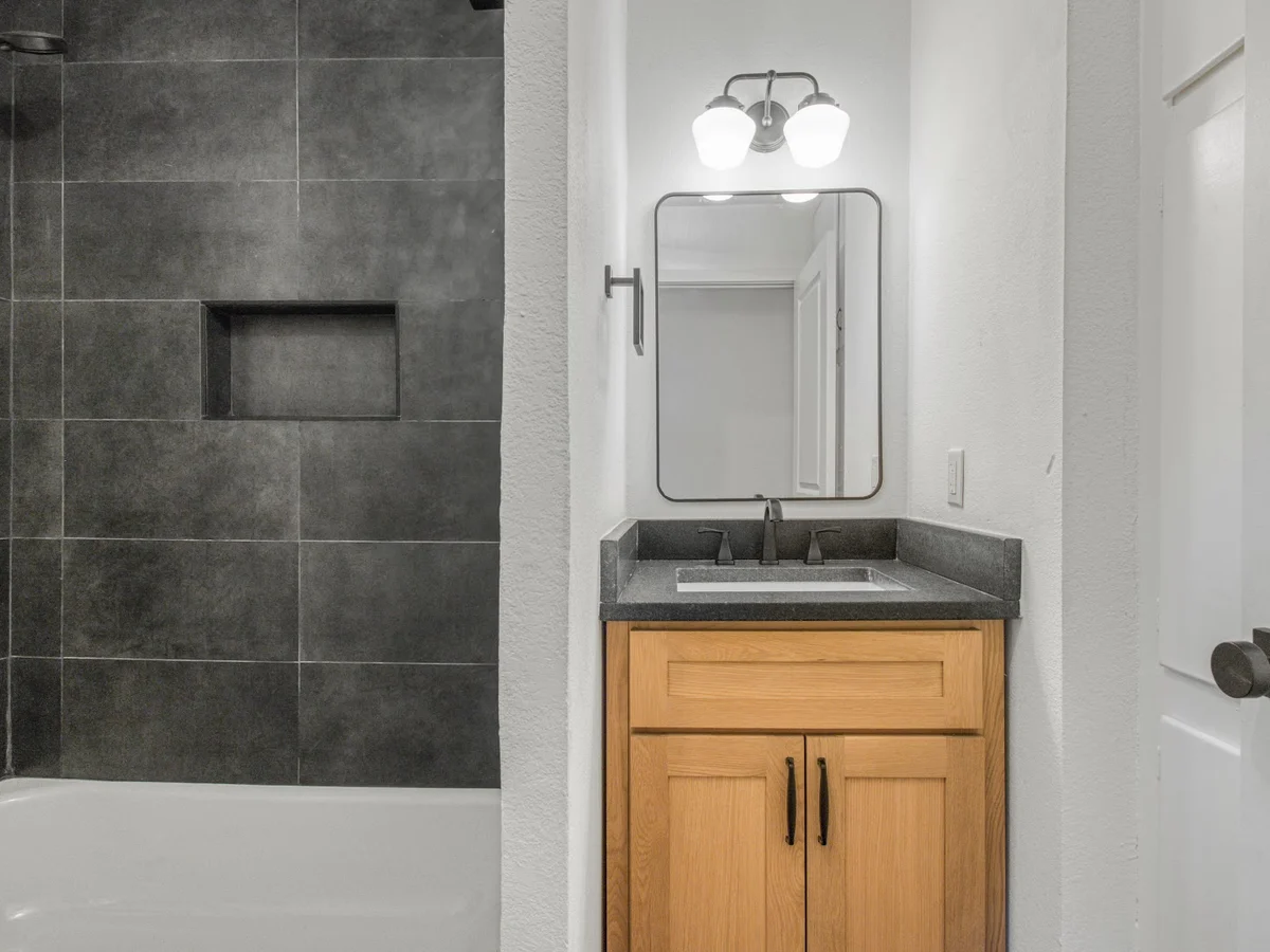 Completed bathroom with dark large format tile and an oak vanity