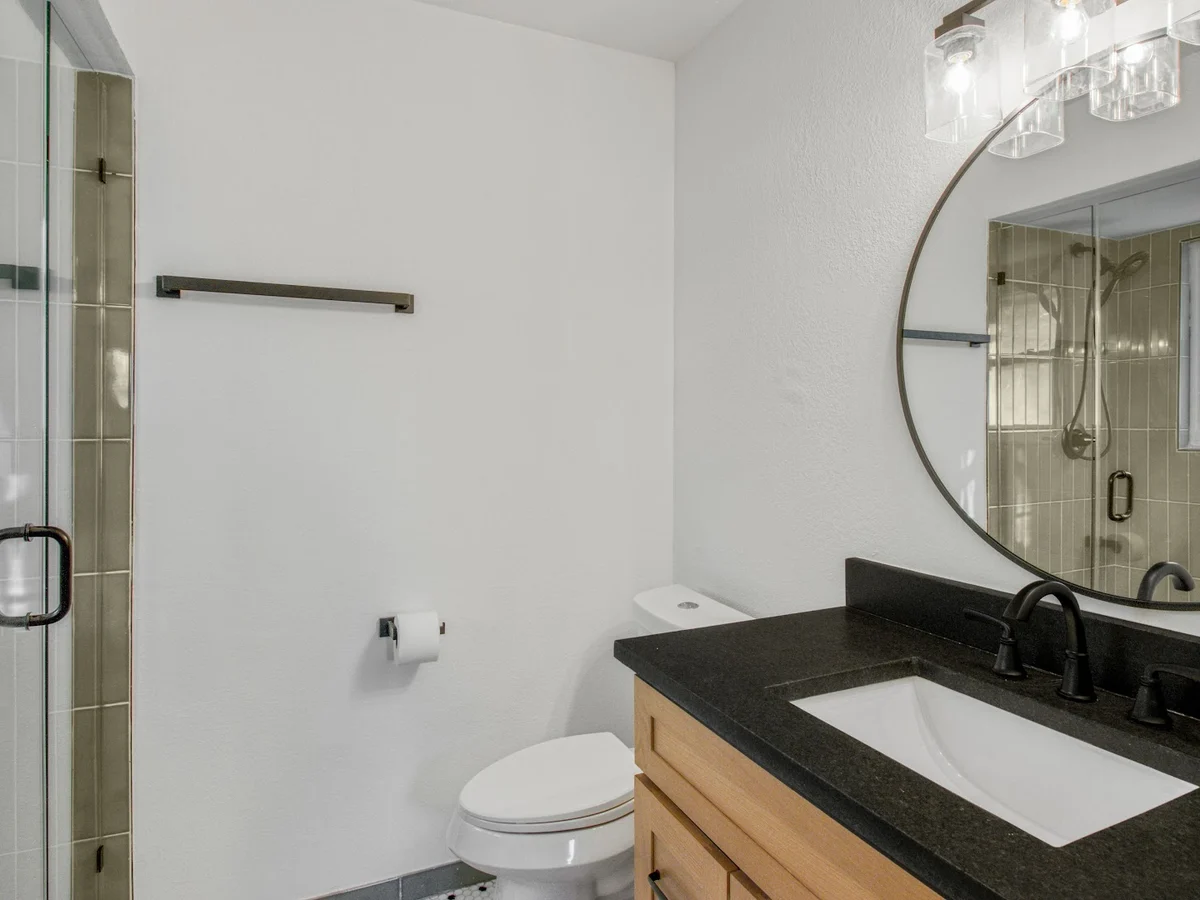 Completed bathroom with a round mirror, dark stone vanity top, and fresh white walls