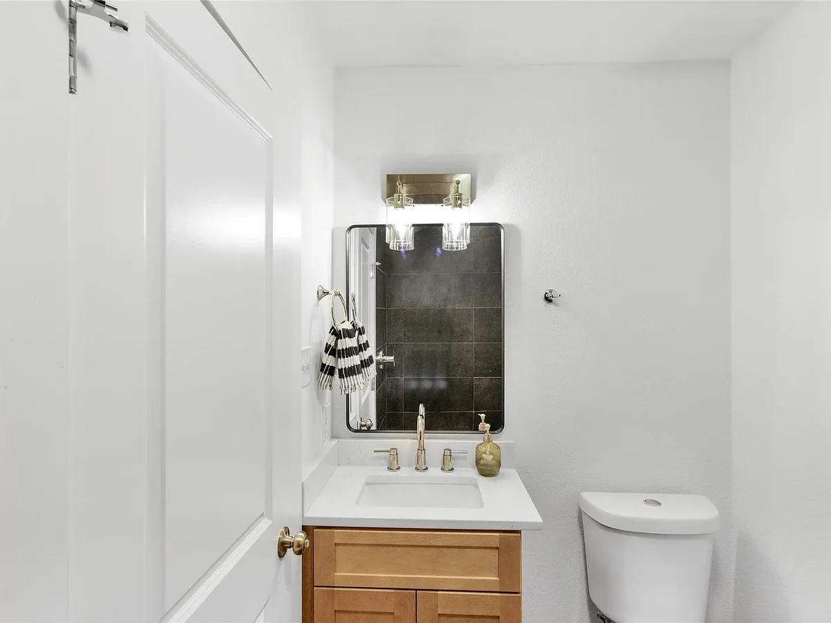 Powder room finished with a dark tile accent wall, oak vanity, and brass fixtures