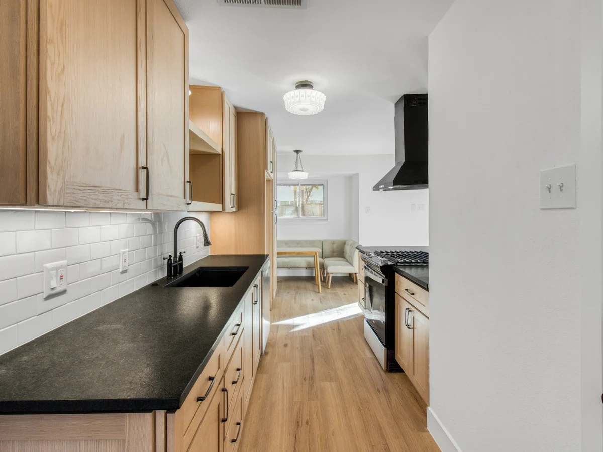 Completed galley kitchen remodel with oak cabinetry, black counters, and a stainless range hood