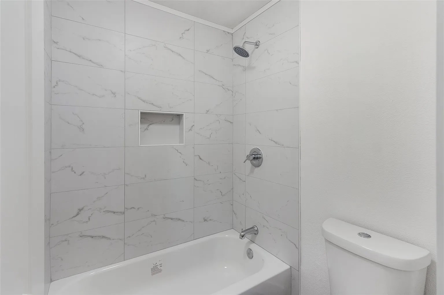 Freshly remodeled bathroom showing chrome shower head, marble tile surround, white soaking tub, and chrome fixtures — Lantern plumbing work in a DFW home