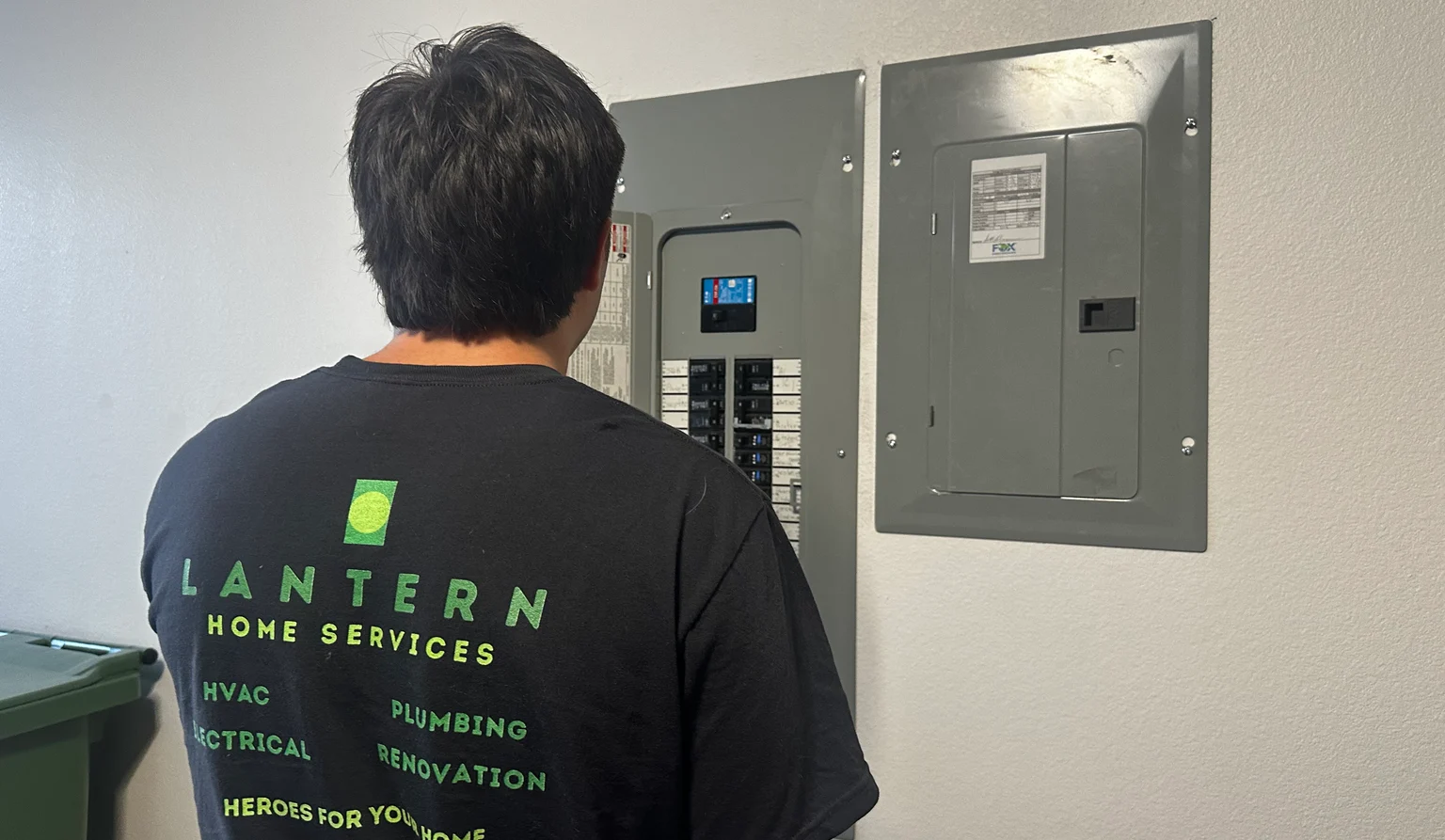 Daryl of Lantern Home Services working at an open residential electrical panel, with Lantern Home Services shirt branding visible